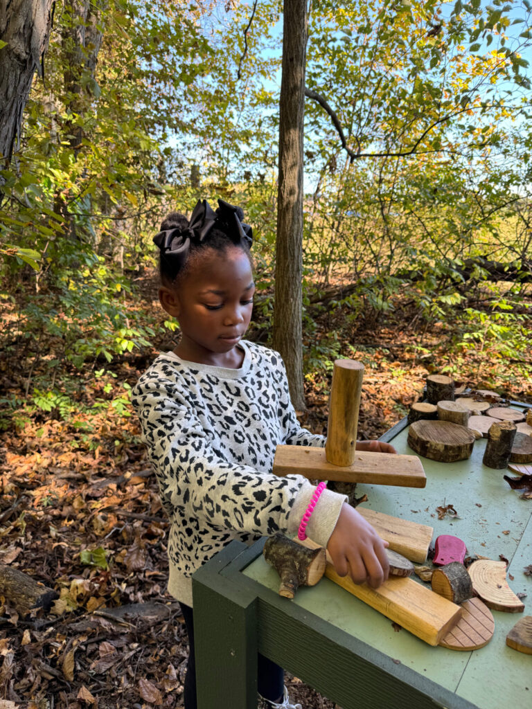 Little girl plays outside in AEP Nature Explore Classroom in Fort Wayne, Ind. with wooden toy blocks.