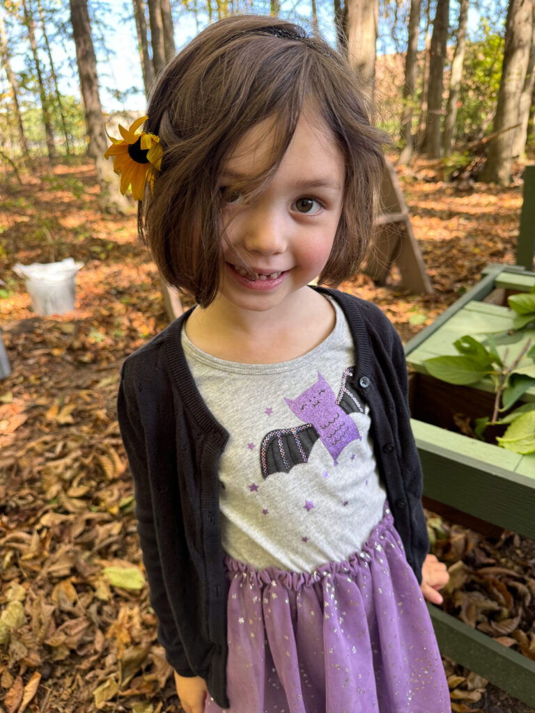 Little girl stands in the outdoor classroom with a yellow flower in her hair.